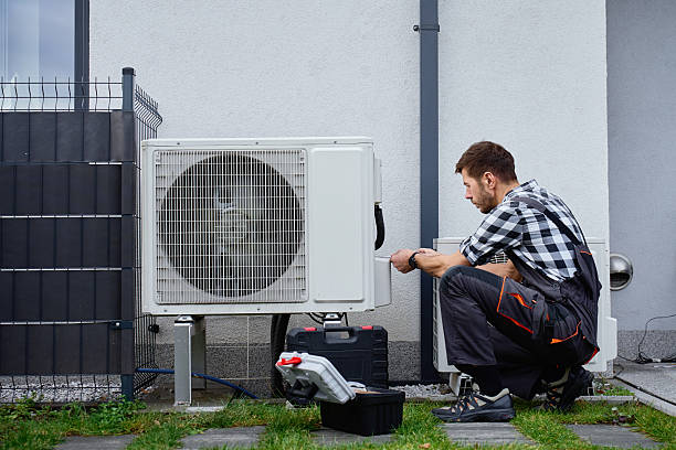 Technician inspecting residential HVAC components during seasonal maintenance in a Mineola utility area, Technician performing HVAC maintenance in an Islip - NY basement while testing airflow at the furnace